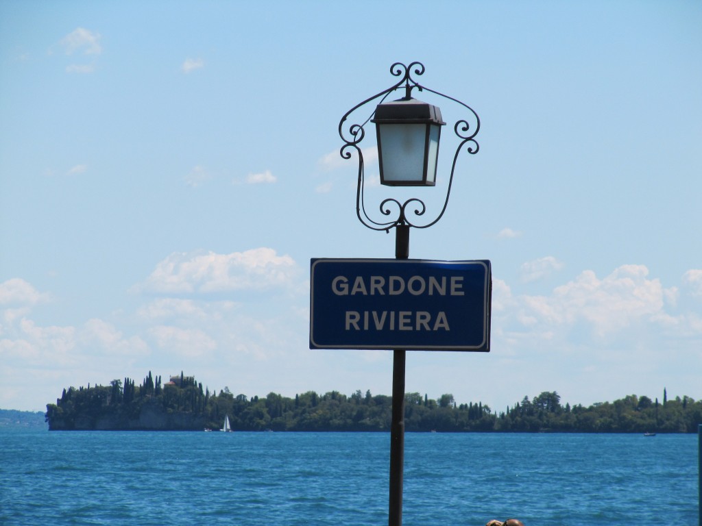 Een naambord van Gardone Riviera met het Gardameer en Isola del Garda op de achtergrond
